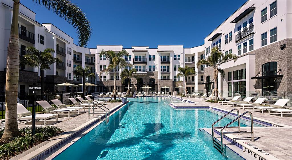 A swimming pool sits in the courtyard of a modern multi-story apartment building with palm trees — 700 AULTMAN STREET UNIT Heritage, KISSIMMEE, FL