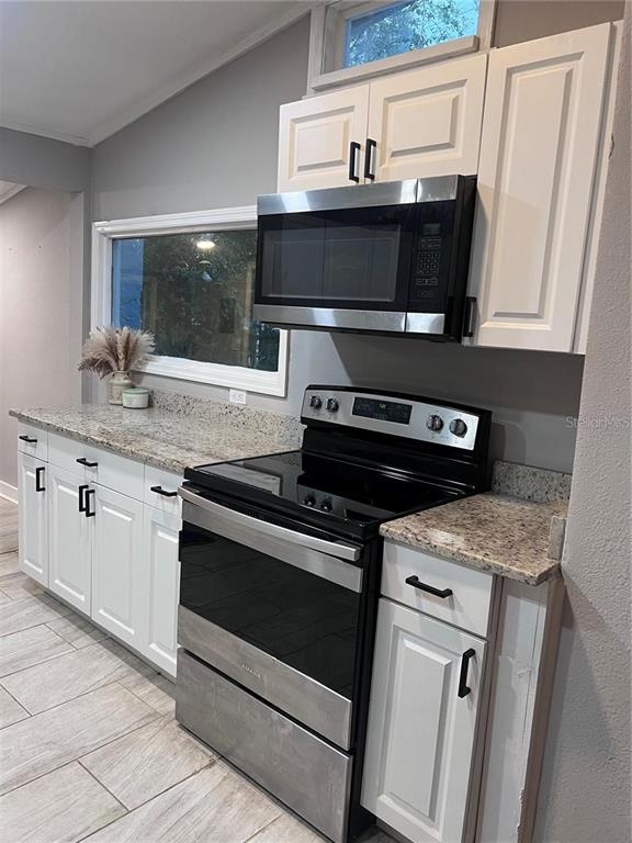 A kitchen features white cabinets, granite countertops, and stainless steel appliances against a gray wall — 1635 PARTRIDGE BOULEVARD, ZEPHYRHILLS, FL