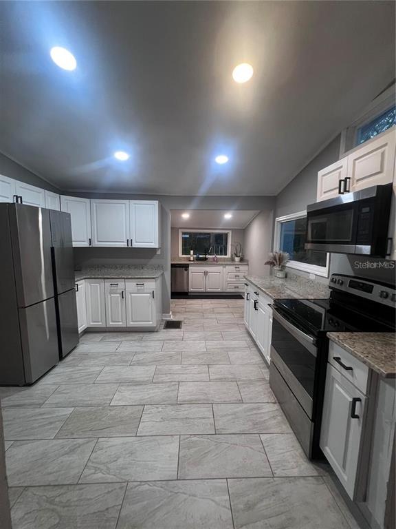 A kitchen features white cabinetry, stainless steel appliances, granite countertops, and light-colored tile flooring — 1635 PARTRIDGE BOULEVARD, ZEPHYRHILLS, FL