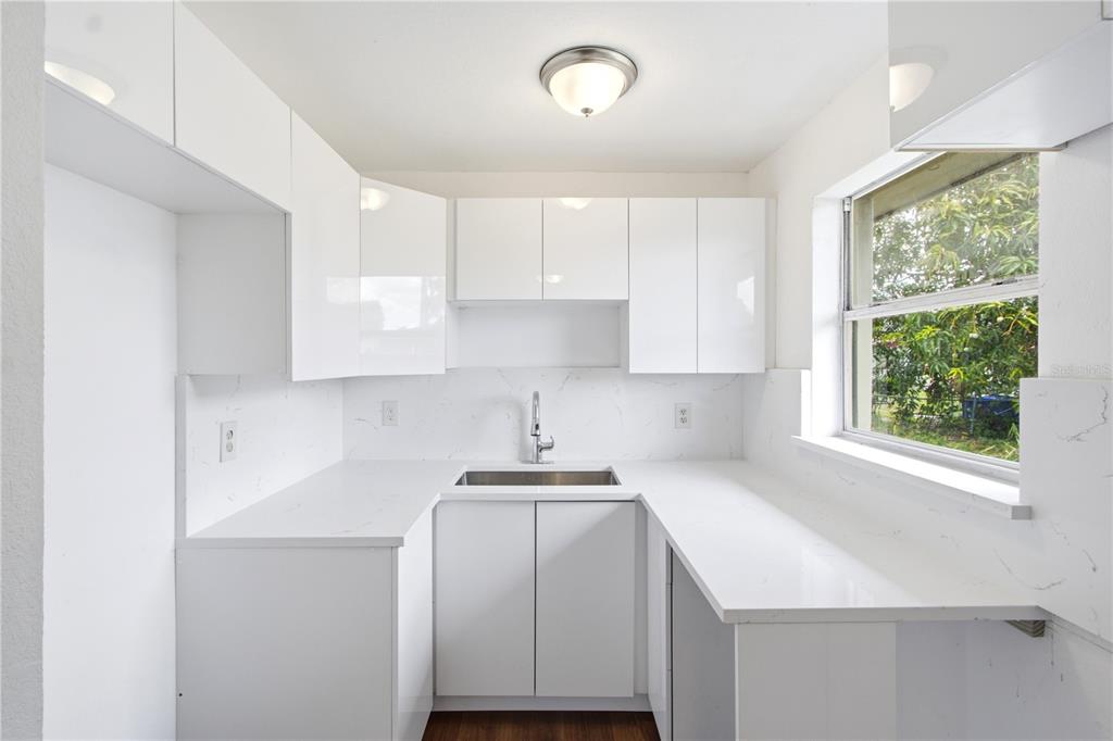 A modern kitchen features white flat-panel cabinets, white quartz countertops, and a stainless steel sink — 1629 PAWNEE STREET, FORT MYERS, FL