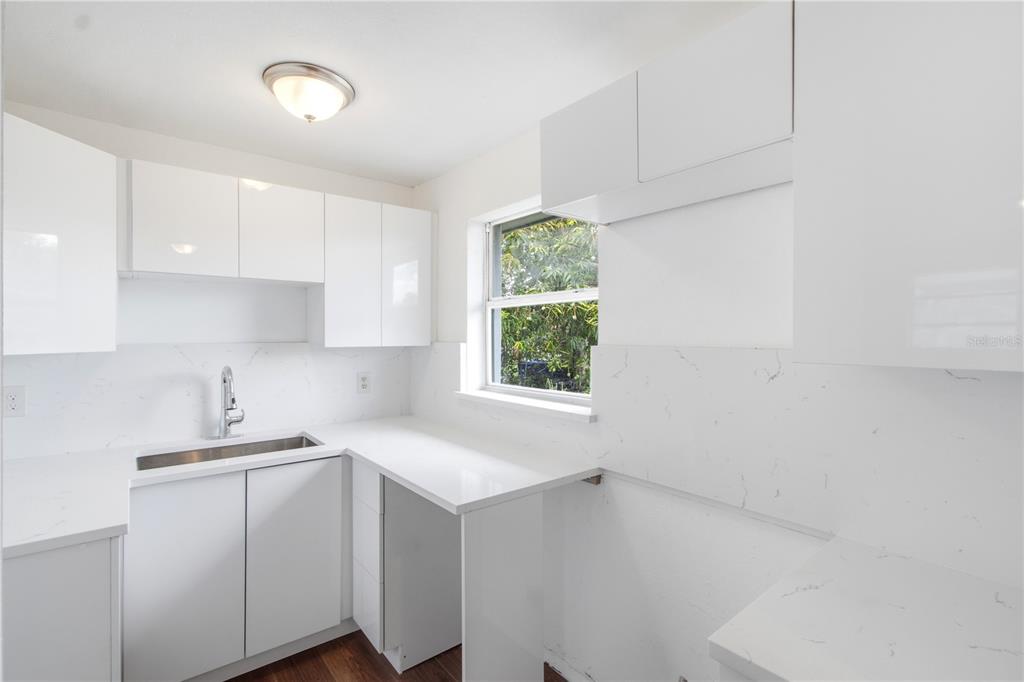 A modern white kitchen features sleek cabinetry, a stainless steel sink, and quartz countertops — 1629 PAWNEE STREET, FORT MYERS, FL