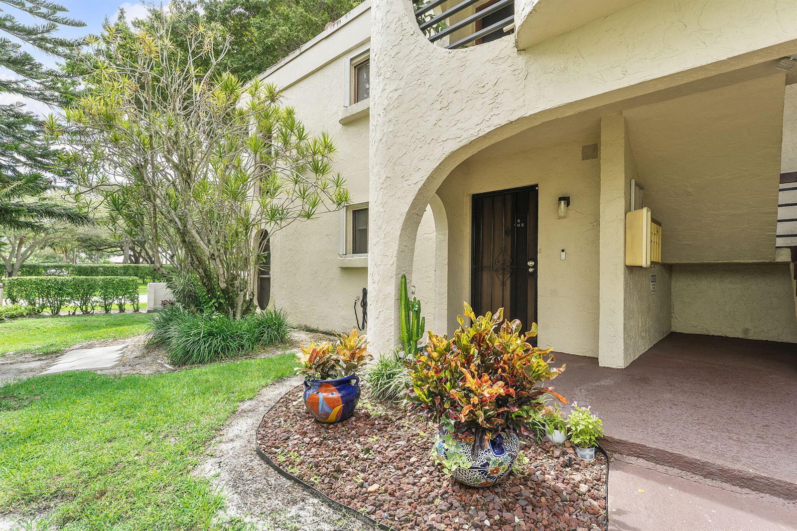 A stucco building exterior features an arched entryway, potted plants, and a landscaped lawn — 6314 Longboat Lane W, Boca Raton FL 33433, BOCA RATON, FL