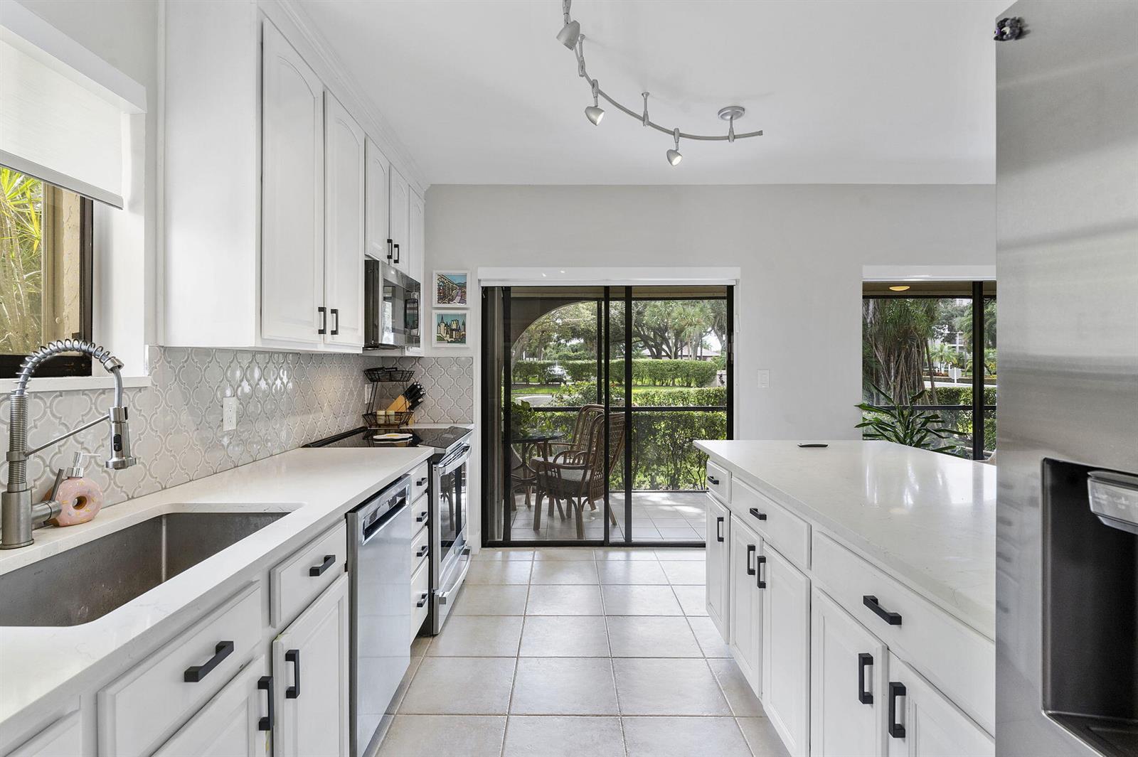 A kitchen features white cabinets, a quartz island with two chairs, and sliding glass doors — 6314 Longboat Lane W, Boca Raton FL 33433, BOCA RATON, FL