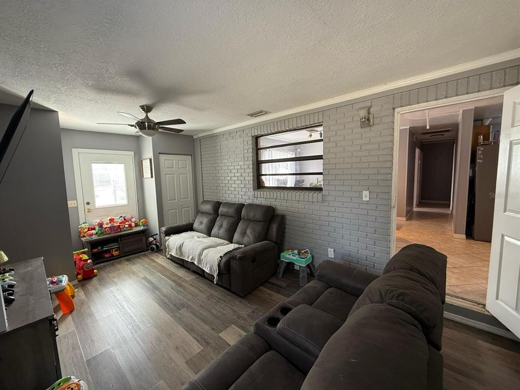 A living room features gray brick walls, wood-look flooring, and two dark brown reclining sofas — 311 CONGRESS AVENUE, AUBURNDALE, FL