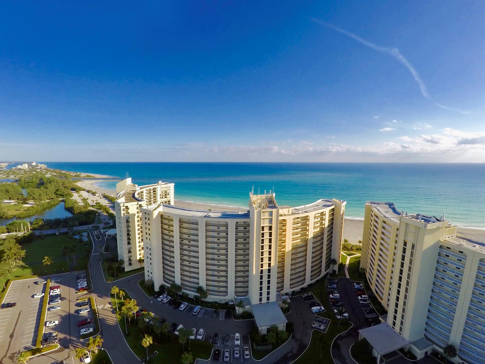 An aerial view of a large, curved beachfront condominium complex with an adjacent parking lot — 300 Ocean Trail Way # 908, Jupiter FL 33477, JUPITER, FL