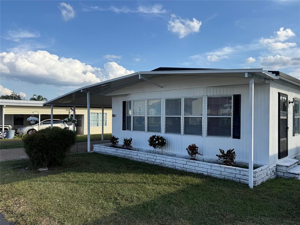 A white mobile home features a carport, a brick planter, and a grassy front yard — 37832 MADEIRA AVENUE, ZEPHYRHILLS, FL