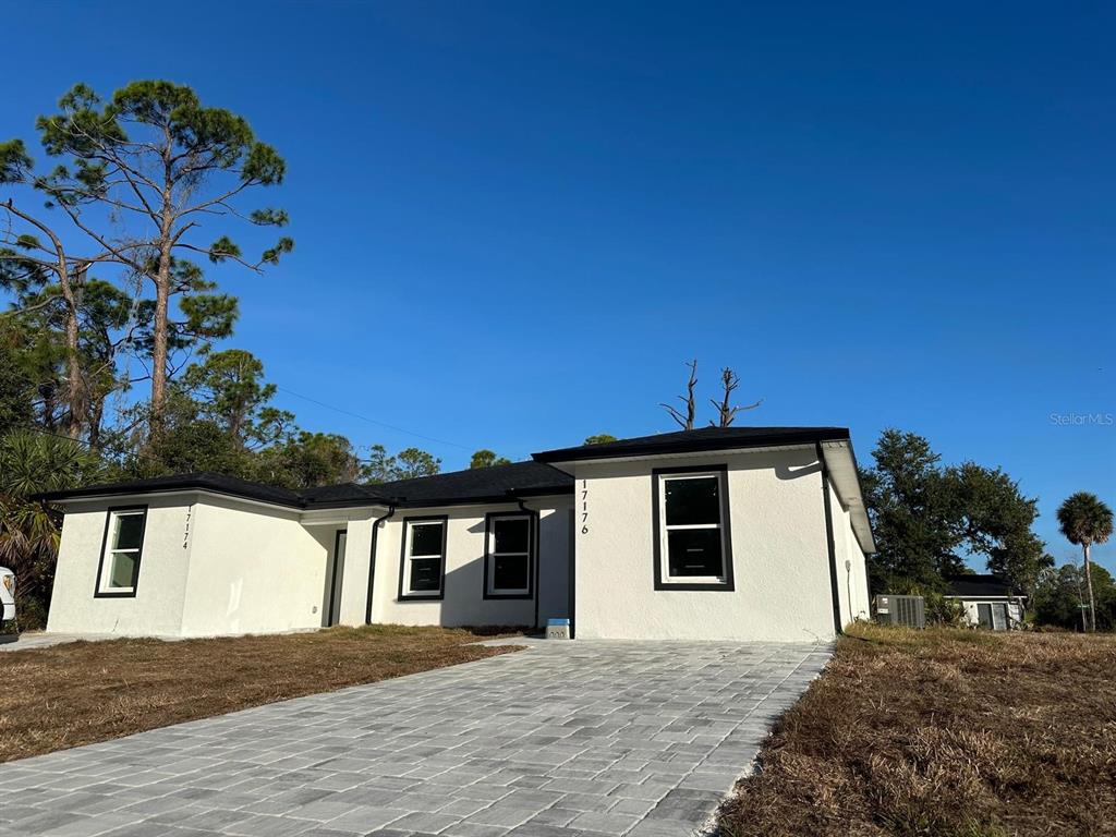 A single-story white house with black trim and a paved driveway under a clear sky — 17174 NIXON AVENUE, PORT CHARLOTTE, FL