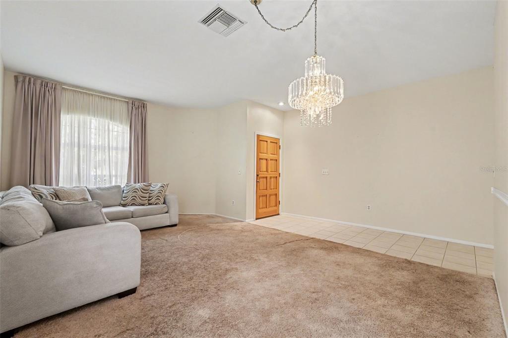 A living room features beige carpet, a crystal chandelier, and a front door entrance — 1714 LARABIE COURT, BRANDON, FL