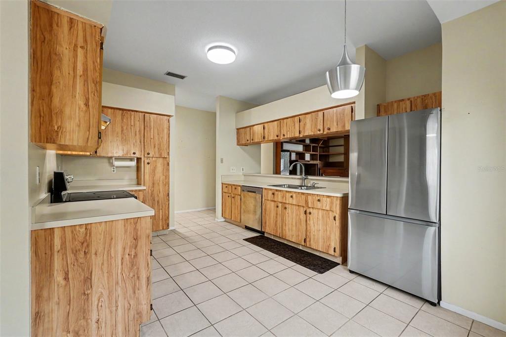 A kitchen features wood-grain cabinets, stainless steel appliances, and light-colored tile flooring — 1714 LARABIE COURT, BRANDON, FL