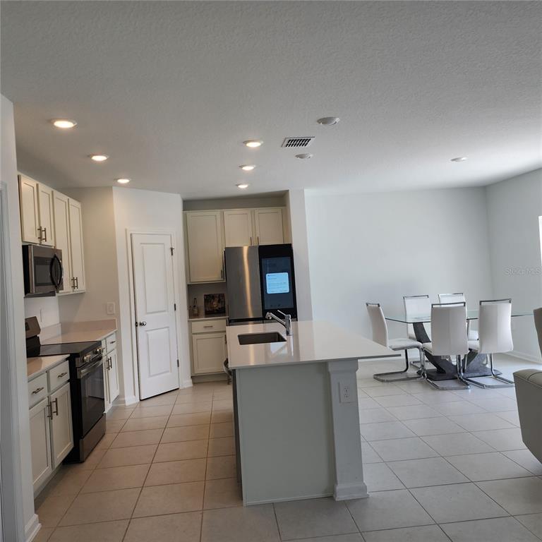 A kitchen features white cabinets, stainless steel appliances, a center island, and a dining area — 5838 LE MARIN WAY, KISSIMMEE, FL