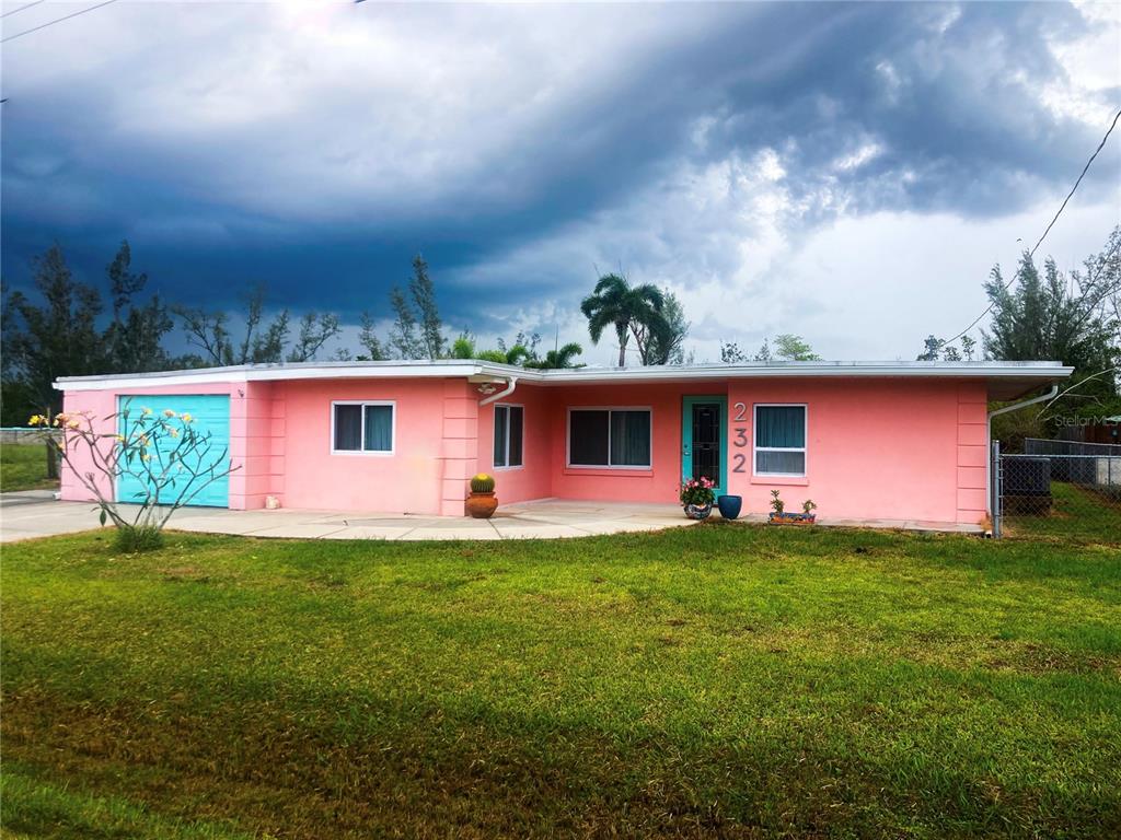 A single-story pink house with a turquoise garage door and front door under a cloudy sky — 232 DARST AVENUE, PUNTA GORDA, FL