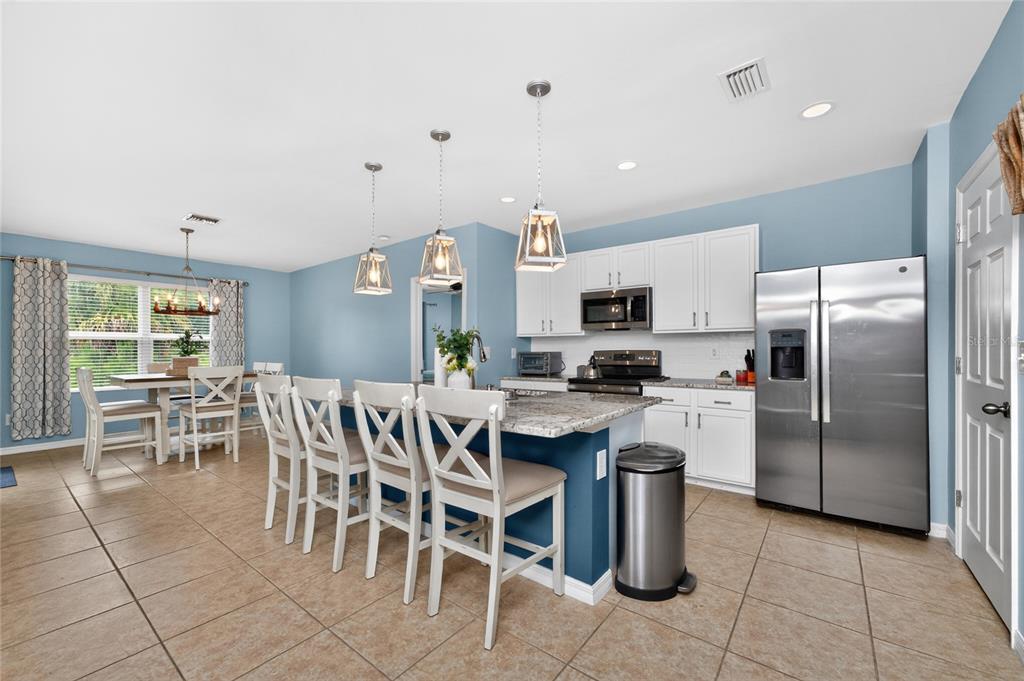 A kitchen with white cabinets, granite countertops, a blue island, and an adjacent dining area — 7164 MIKASA DRIVE, PUNTA GORDA, FL