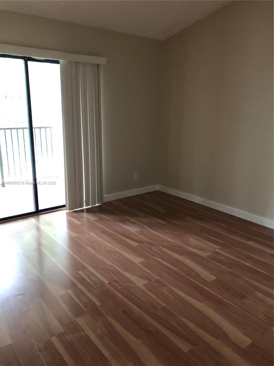 An empty room features wood-look flooring, beige walls, and a sliding glass door with blinds — 620 S Park Rd # 2, Hollywood FL 33021, HOLLYWOOD, FL