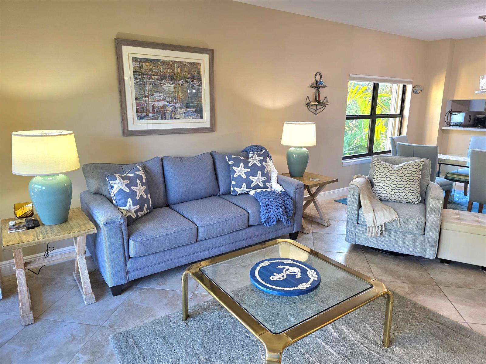 A living room features a blue sofa, a glass-topped coffee table, and coastal-themed decor — 300 Uno Lago Drive # 305, Juno Beach FL 33408, JUNO BEACH, FL