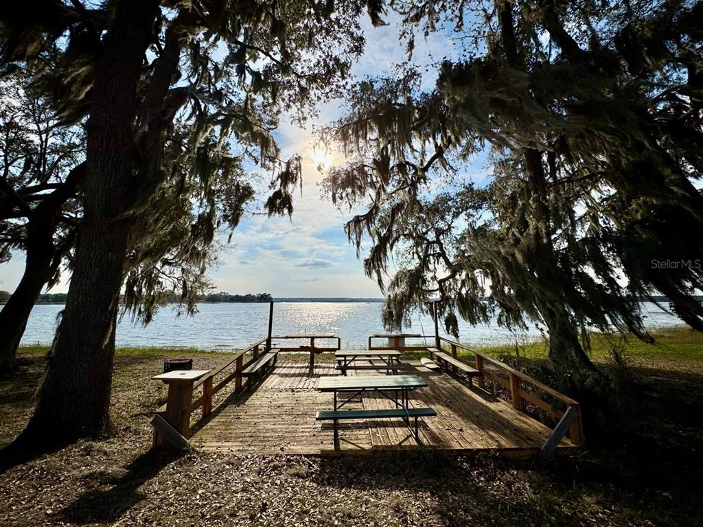 A wooden deck with picnic tables sits under mossy oak trees overlooking a lake — 25232 NE 143RD STREET UNIT 178, SALT SPRINGS, FL