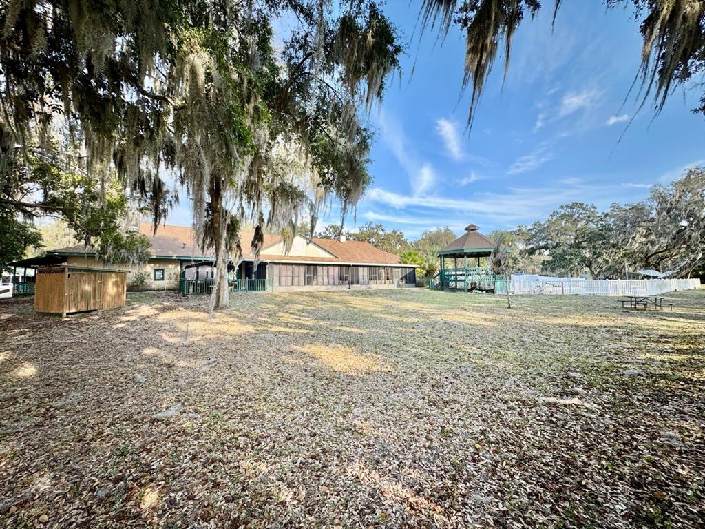 A large backyard features a house with a screened porch, a gazebo, and mature trees — 25232 NE 143RD STREET UNIT 178, SALT SPRINGS, FL