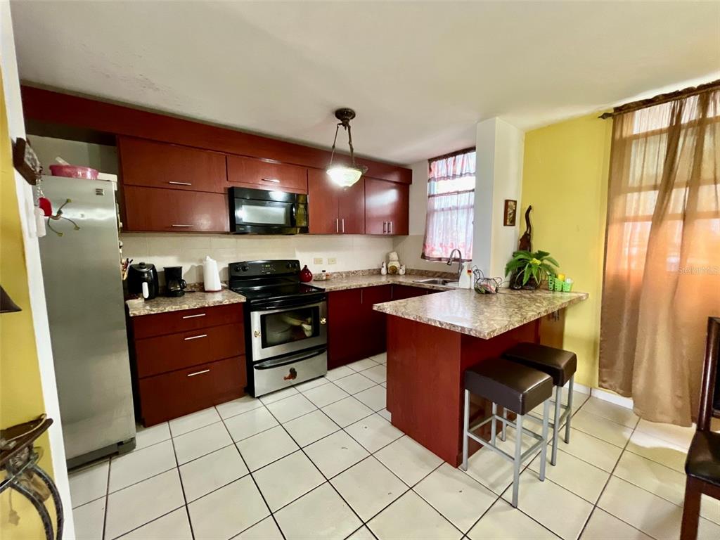 A kitchen features dark wood cabinets, stainless steel appliances, a breakfast bar, and tiled floors — Cond. La Loma B-104 UNIT 104, FAJARDO, PR