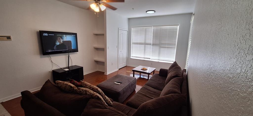 A living room features a wall-mounted television, a brown sectional sofa, and built-in shelving — 8927 LEGACY COURT UNIT 201, KISSIMMEE, FL