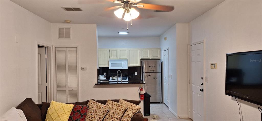 A living room opens to a kitchen with light cabinets, stainless appliances, and a breakfast bar — 8927 LEGACY COURT UNIT 201, KISSIMMEE, FL