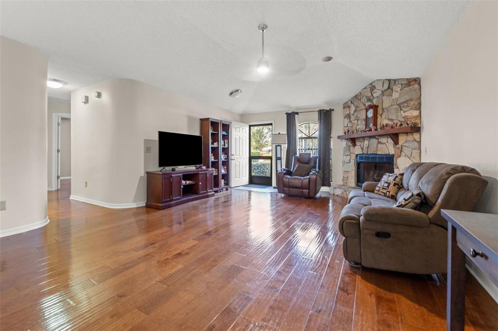 A living room with hardwood floors, a stone fireplace, and a television on a stand — 23315 CLUB VILLAS DRIVE, LAND O LAKES, FL