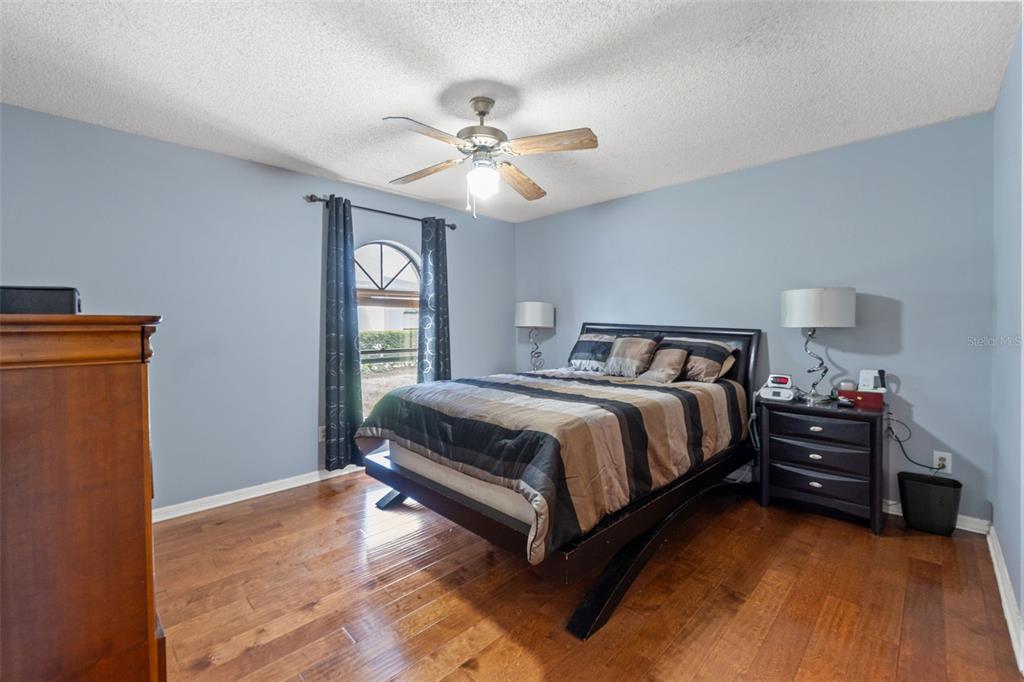 A bedroom features light blue walls, hardwood floors, a ceiling fan, and a dark bed frame — 23315 CLUB VILLAS DRIVE, LAND O LAKES, FL