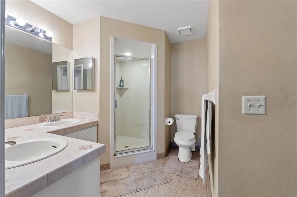A bathroom features a double vanity with tiled countertops, a glass shower, and a toilet — 23315 CLUB VILLAS DRIVE, LAND O LAKES, FL