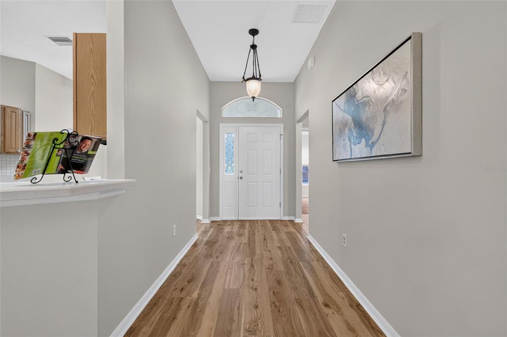 A bright entryway features wood-look flooring, a white front door, and a hanging pendant light — 17101 SE 94TH BERRIEN COURT, THE VILLAGES, FL
