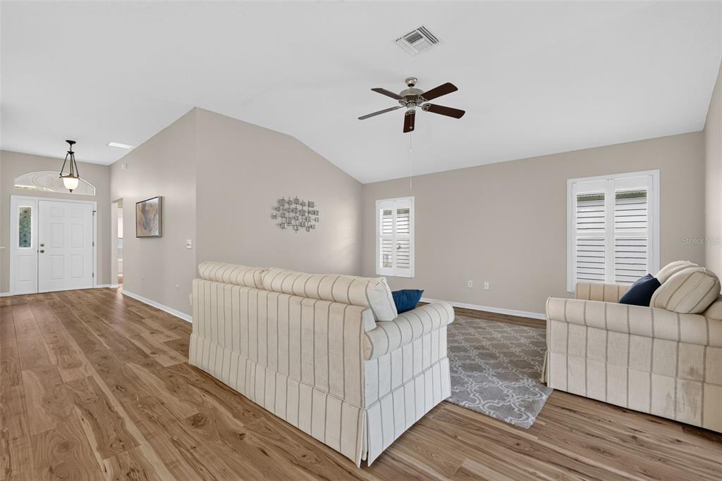 A living room features light-colored walls, wood-look flooring, two striped sofas, and a ceiling fan — 17101 SE 94TH BERRIEN COURT, THE VILLAGES, FL