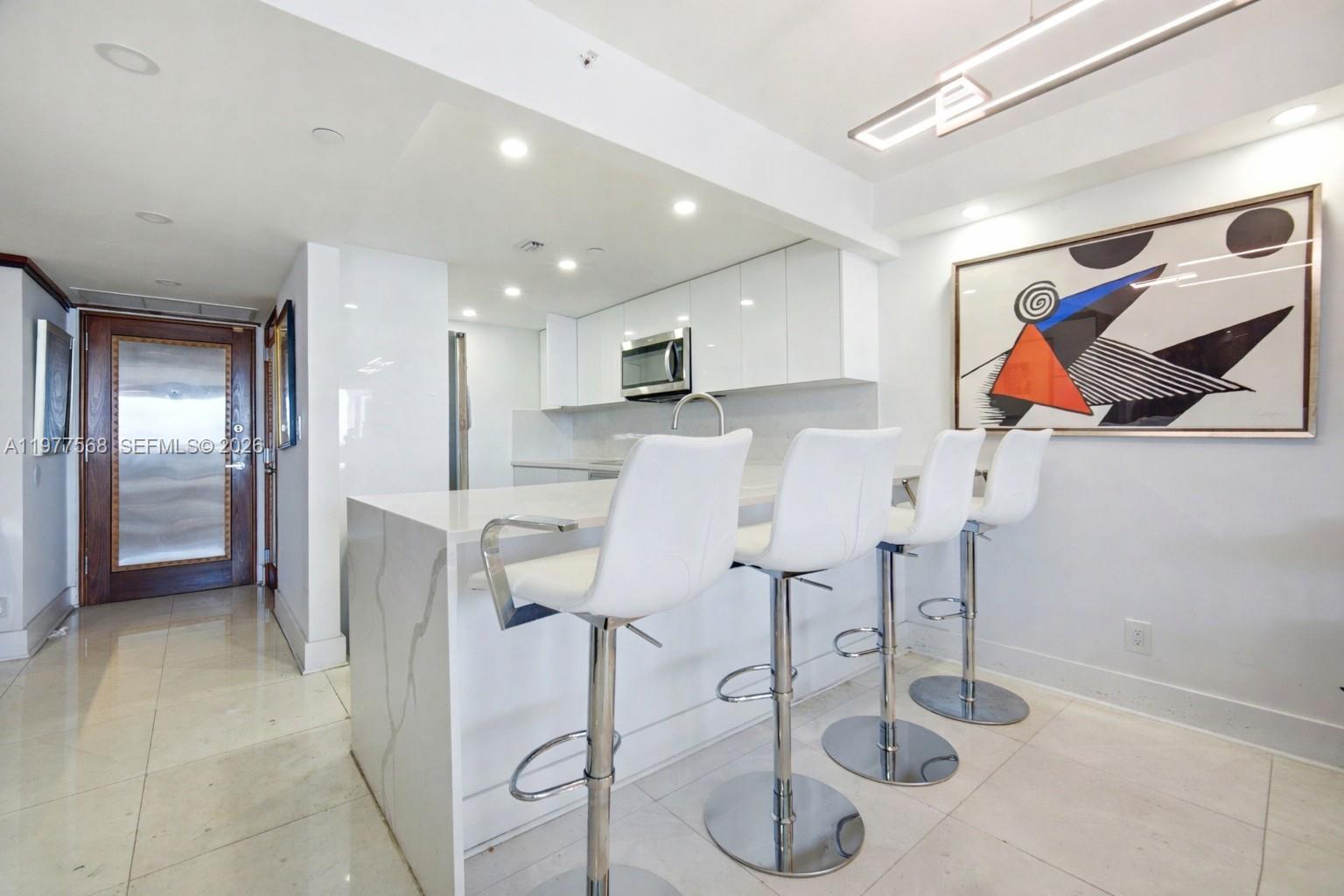 A modern kitchen features a white quartz island with four bar stools and white cabinetry — 1717 N Bayshore Dr # 3354, Miami FL 33132, MIAMI, FL