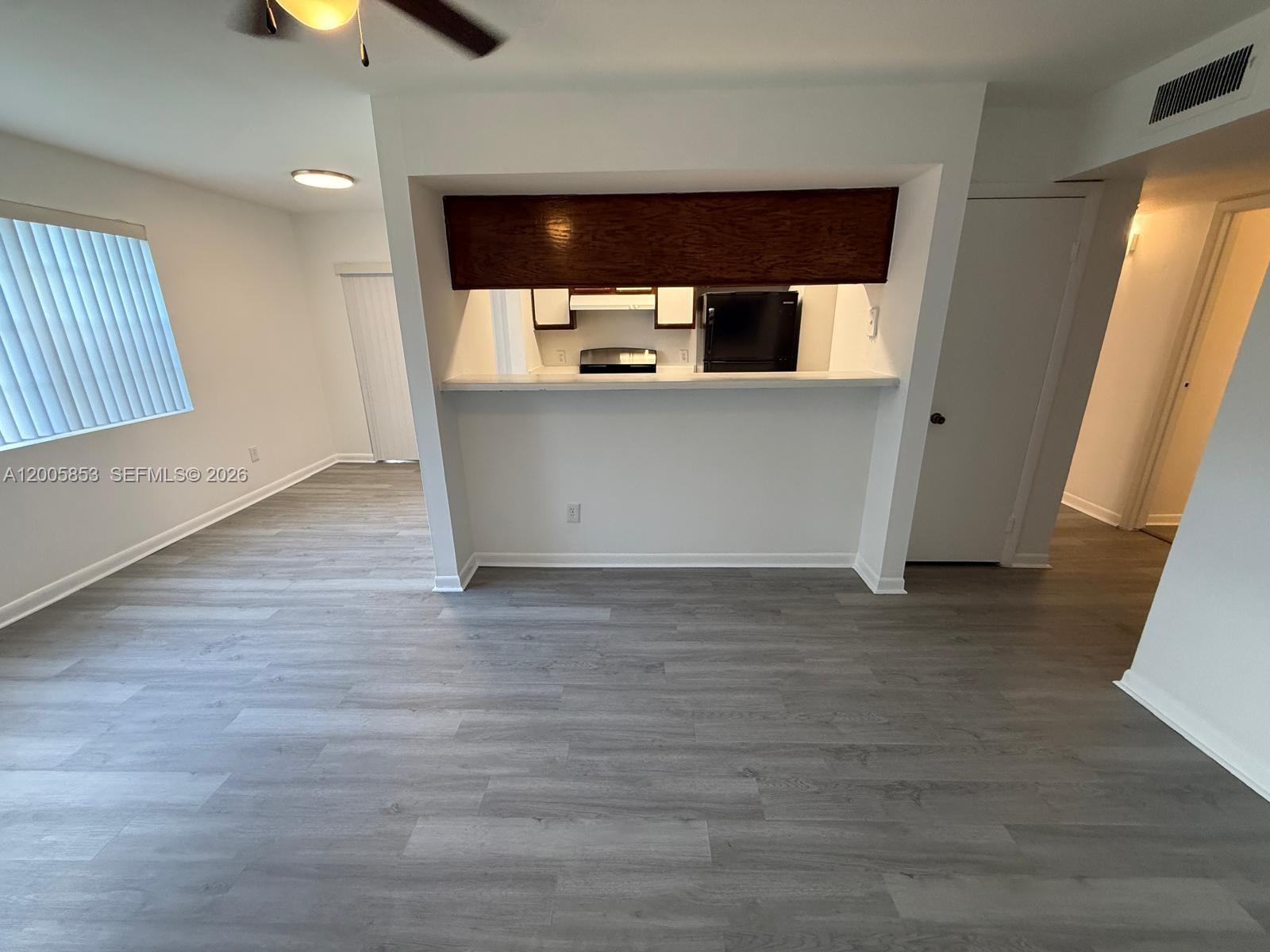 A living area features gray wood-look flooring, white walls, and a kitchen pass-through window — 15285 SW 107th Ln # 214, Miami FL 33196, MIAMI, FL
