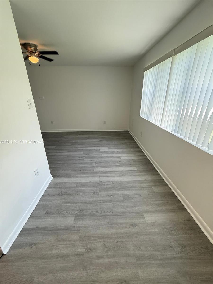 An empty room features gray wood-look flooring, white walls, and vertical window blinds — 15285 SW 107th Ln # 214, Miami FL 33196, MIAMI, FL