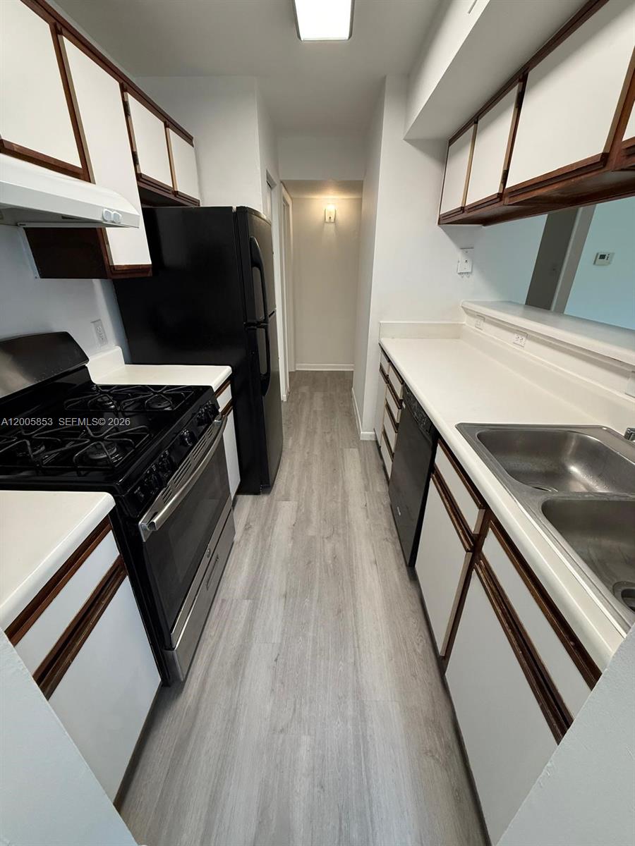 A galley kitchen features white cabinets, black appliances, and light wood-look flooring — 15285 SW 107th Ln # 214, Miami FL 33196, MIAMI, FL