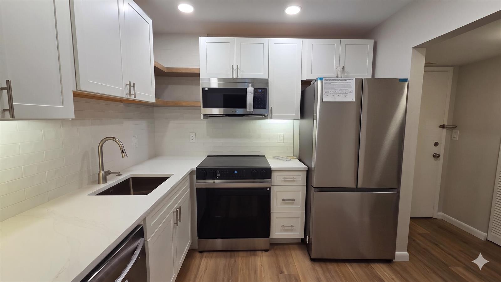 A modern kitchen features white cabinets, stainless steel appliances, light countertops, and wood-look flooring — 257 S Cypress Road # 408, Pompano Beach FL 33060, POMPANO BEACH, FL