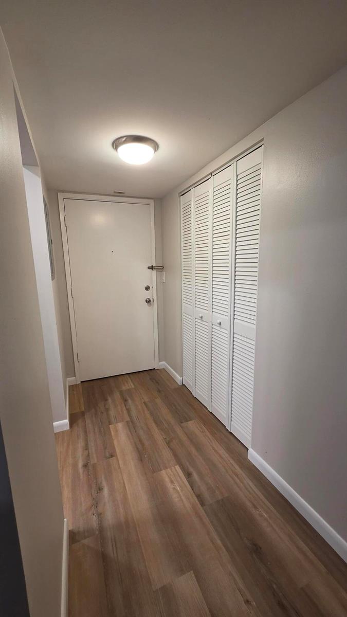 A hallway features light wood-look flooring, a white entry door, and white louvered closet doors — 257 S Cypress Road # 408, Pompano Beach FL 33060, POMPANO BEACH, FL