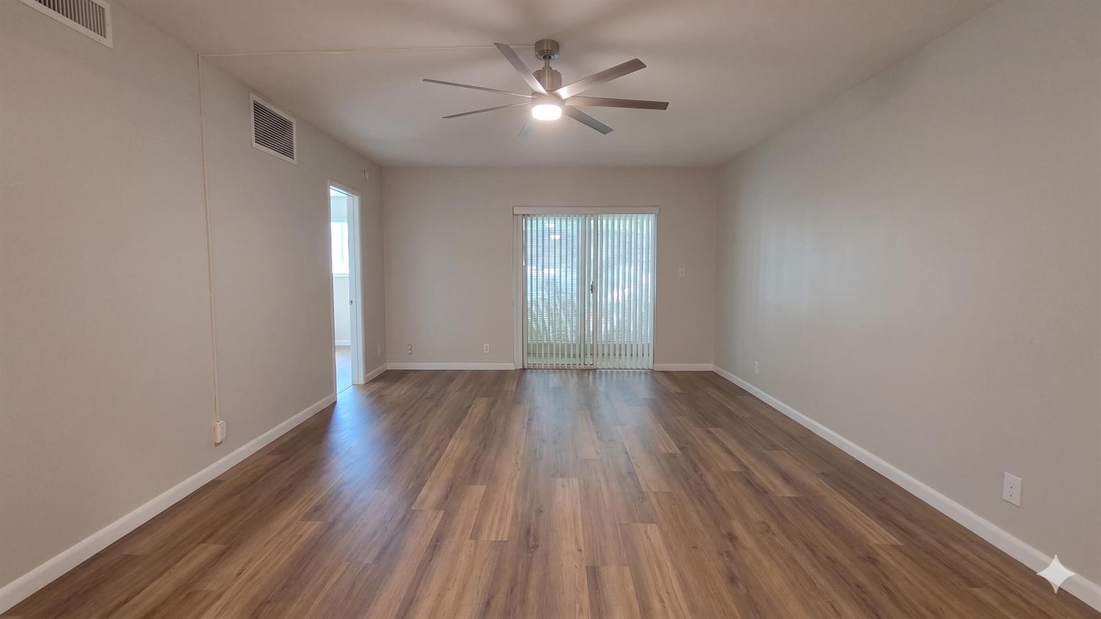 An empty living room features wood-look flooring, a ceiling fan, and sliding glass patio doors — 257 S Cypress Road # 408, Pompano Beach FL 33060, POMPANO BEACH, FL