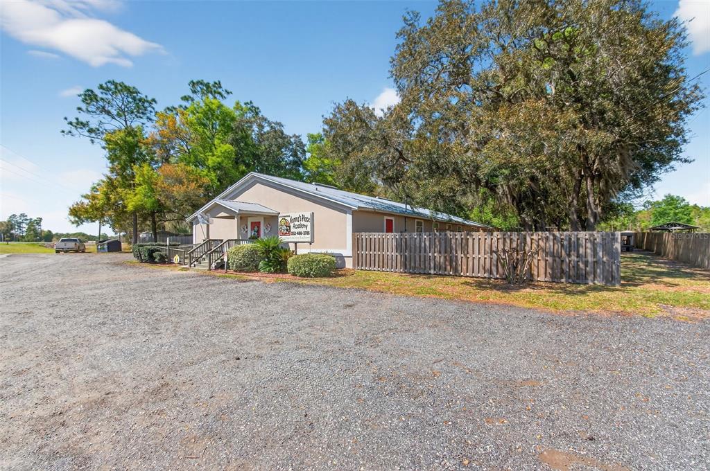 A gravel parking lot leads to a single-story building with a wooden fence and trees — 951 E HATHAWAY AVENUE, BRONSON, FL
