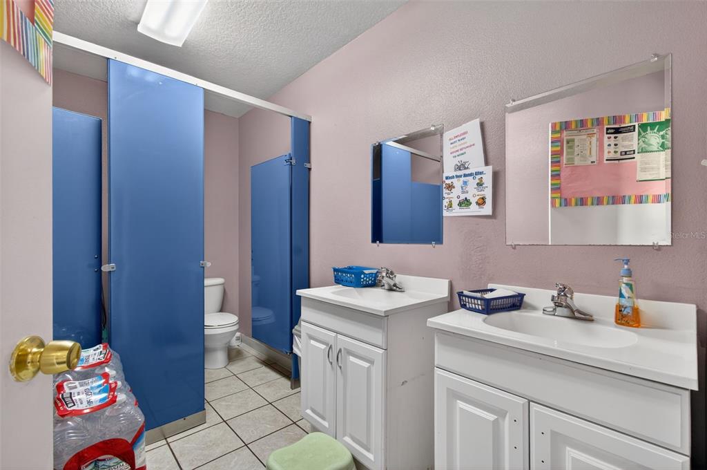A commercial bathroom features two white vanities, blue stall doors, and light-colored tile flooring — 951 E HATHAWAY AVENUE, BRONSON, FL