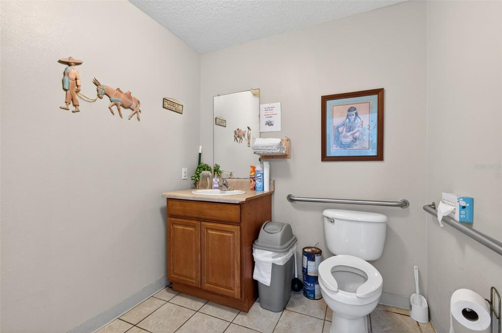 A bathroom with a wooden vanity, a toilet with grab bars, and tiled flooring — 951 E HATHAWAY AVENUE, BRONSON, FL