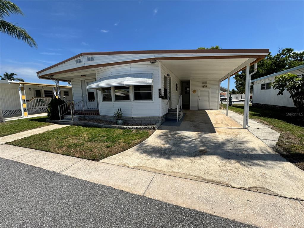 A white mobile home with a carport, a small front lawn, and a concrete driveway — 2331 BELLEAIR RD Lot 237, CLEARWATER, FL