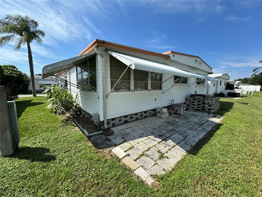 The exterior of a mobile home features a metal awning, siding, and a stone patio — 2331 BELLEAIR RD Lot 237, CLEARWATER, FL