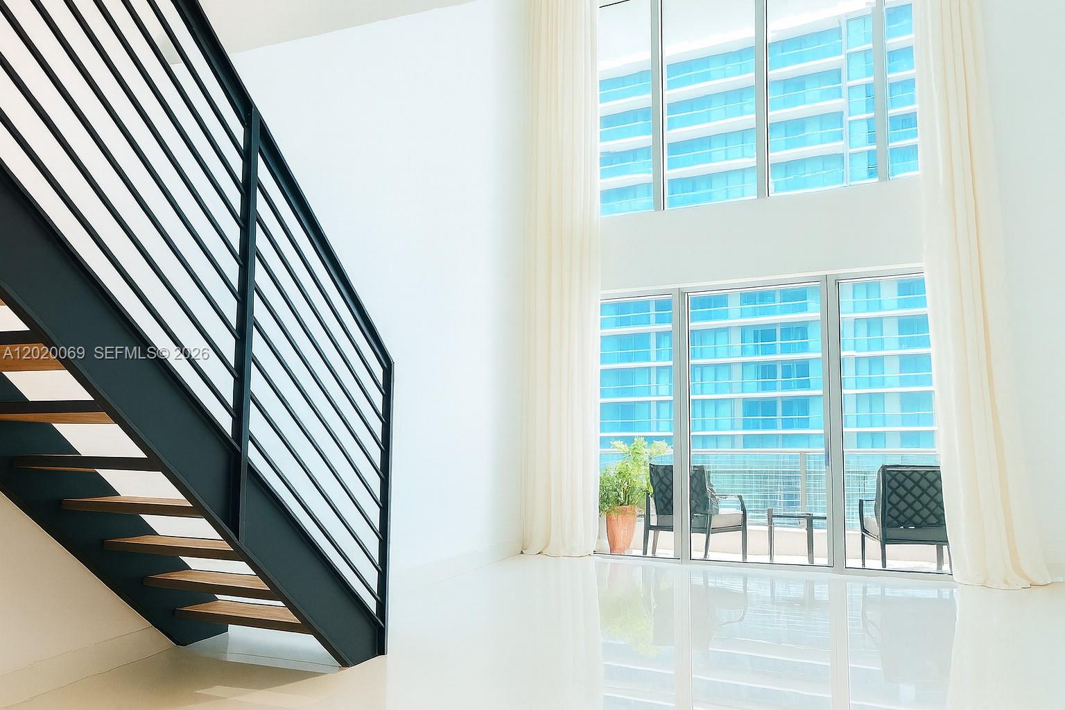 A modern staircase with black railings stands next to floor-to-ceiling windows overlooking a balcony — 60 SW 13th St # 3418, Miami FL 33130, MIAMI, FL