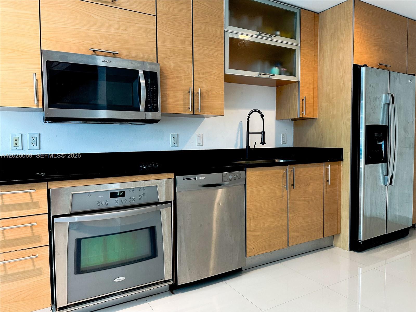 A modern kitchen features light wood cabinetry, stainless steel appliances, and a black countertop — 60 SW 13th St # 3418, Miami FL 33130, MIAMI, FL