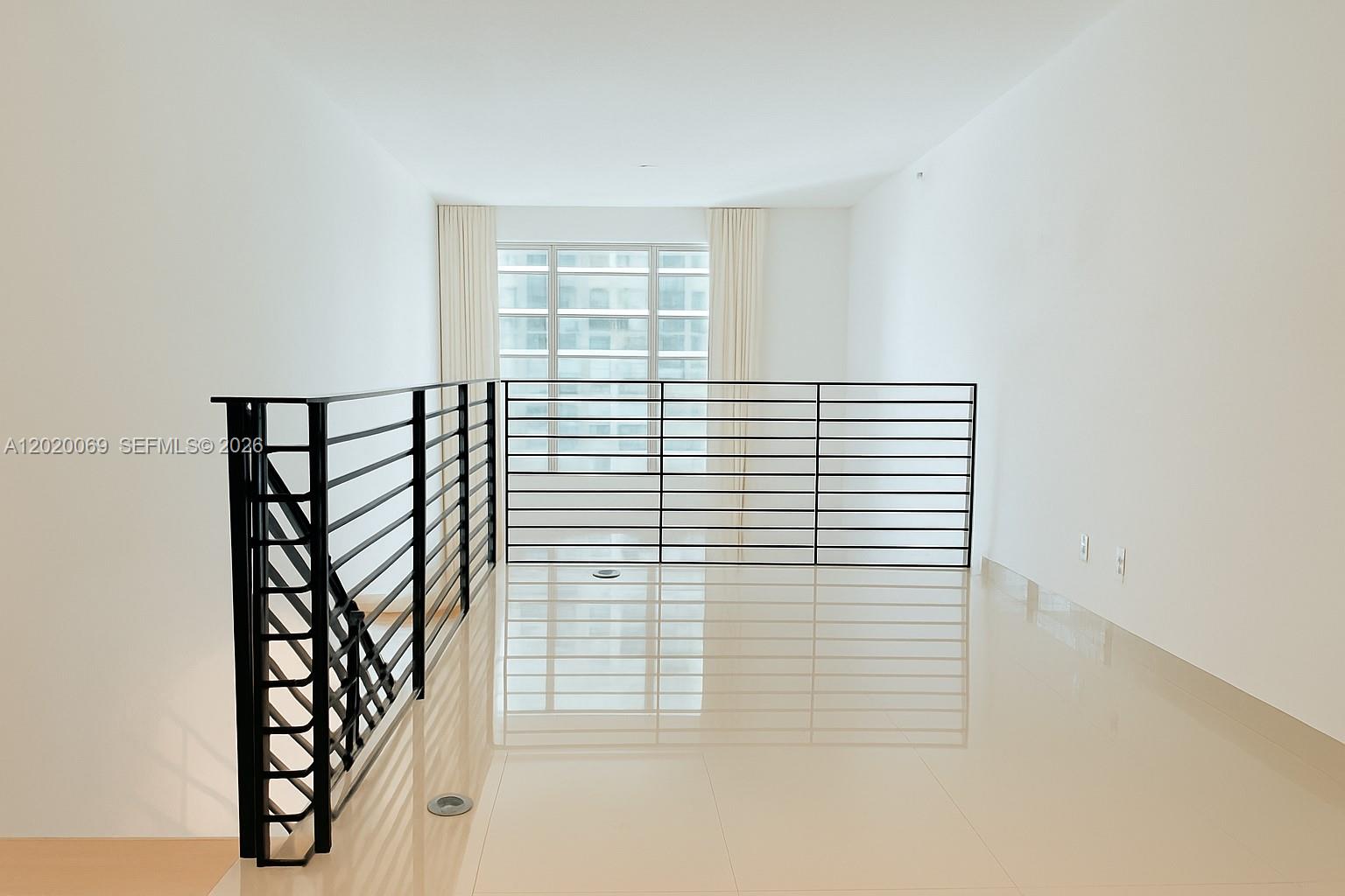 A bright loft space features white walls, polished tile floors, and a black metal railing — 60 SW 13th St # 3418, Miami FL 33130, MIAMI, FL