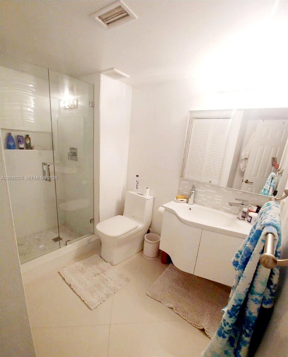 A bathroom features a glass-enclosed shower, a white vanity, and a toilet on tiled floors — WESTON, FL