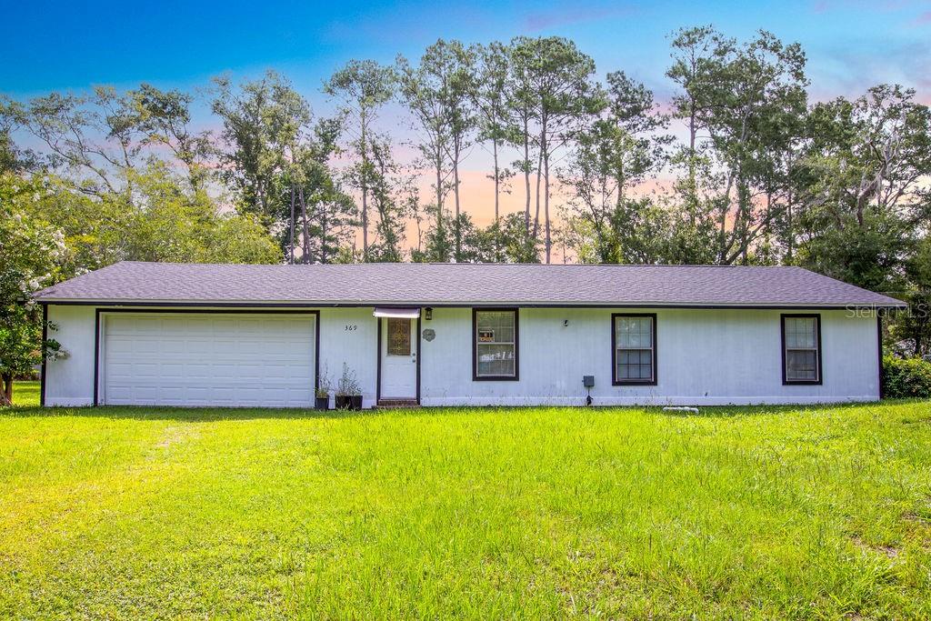 A single-story house with white siding, a garage, and dark trim sits on a lawn — 369 NE DIANA TERRACE, LAKE CITY, FL