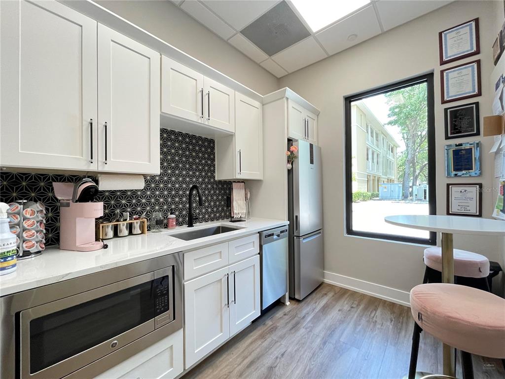 A kitchen features white cabinets, a patterned backsplash, stainless steel appliances, and a window view — 9144 SW 49 PLACE UNIT 101, GAINESVILLE, FL