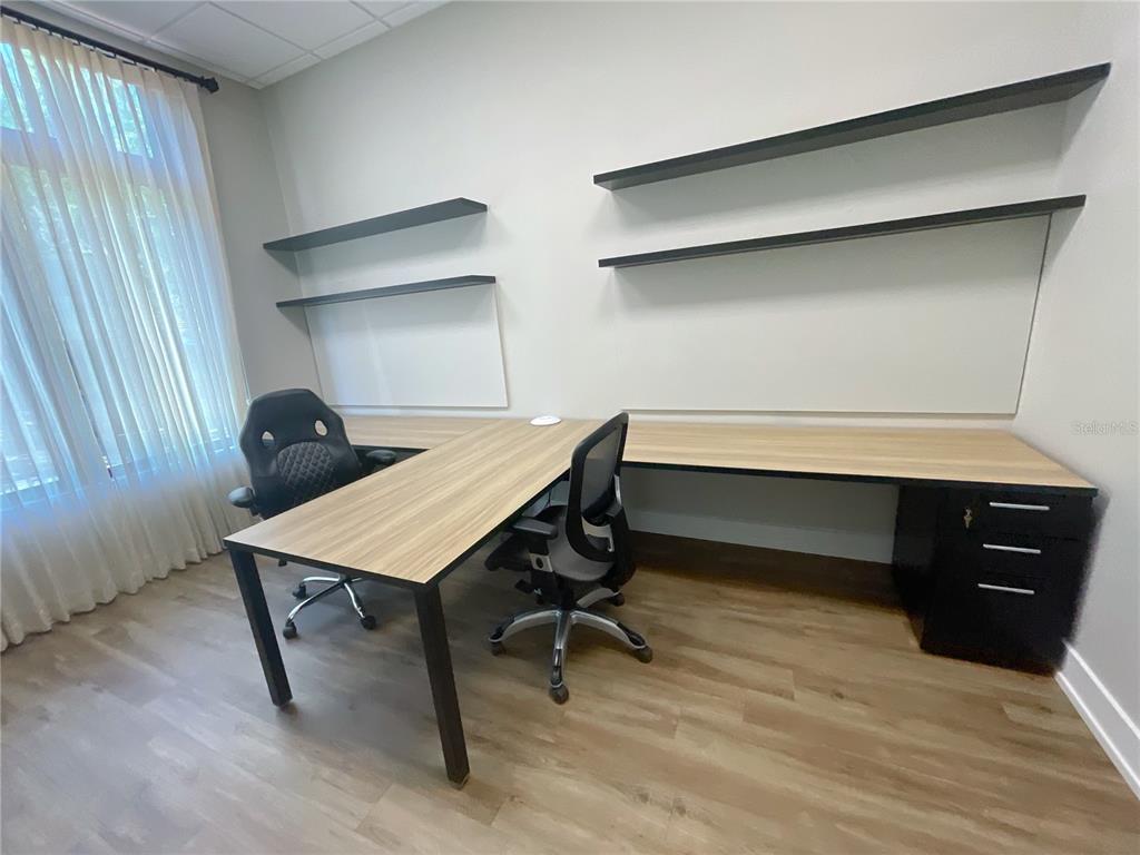 An office room features a wooden L-shaped desk, two chairs, and wall-mounted shelving — 9144 SW 49 PLACE UNIT 101, GAINESVILLE, FL