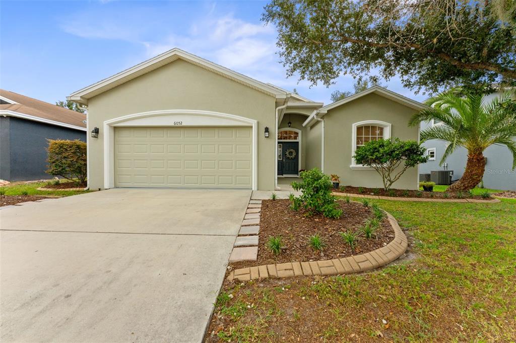 A single-story house with a beige stucco exterior, a two-car garage, and a landscaped front yard — 6052 CHAMPIONS GATE BOULEVARD, ZEPHYRHILLS, FL