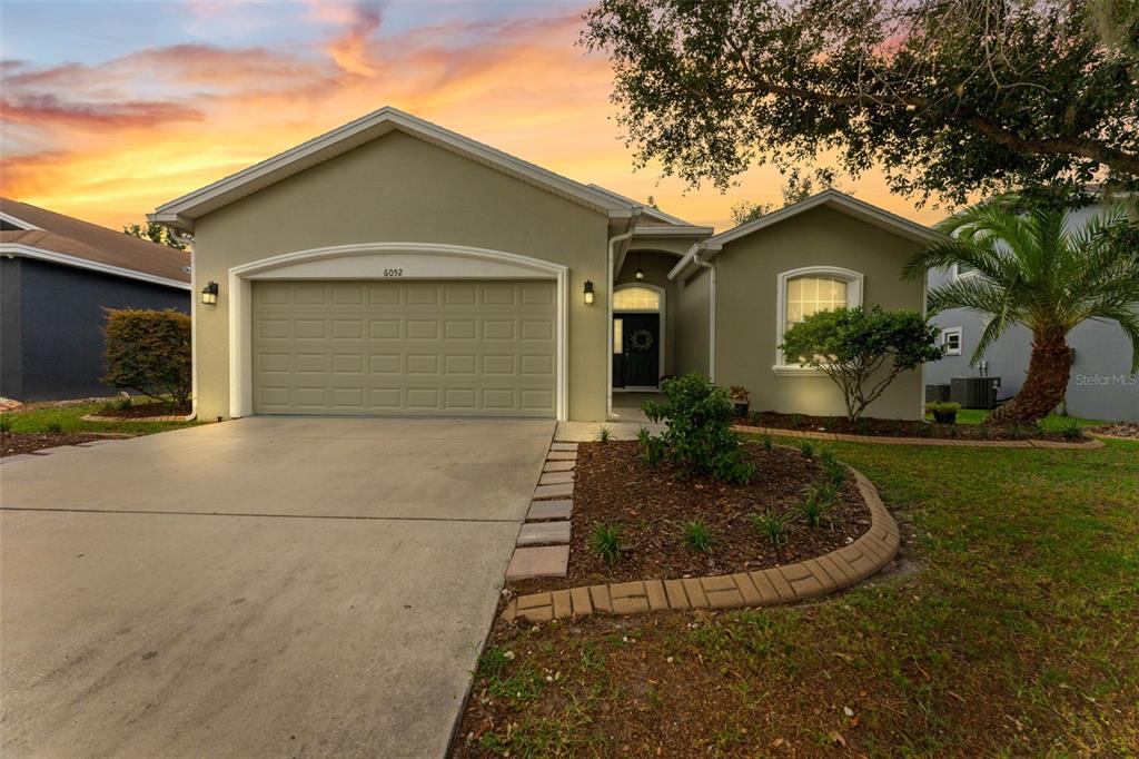 A single-story house with a beige exterior, a two-car garage, and a landscaped front yard — 6052 CHAMPIONS GATE BOULEVARD, ZEPHYRHILLS, FL