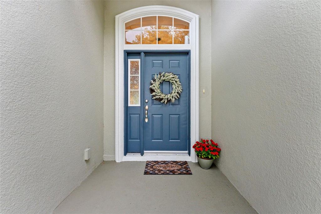 A blue front door with a wreath and sidelight sits under an arched transom window — 6052 CHAMPIONS GATE BOULEVARD, ZEPHYRHILLS, FL
